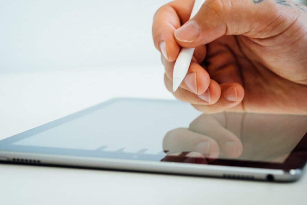 Hand holding a stylus above a tablet.