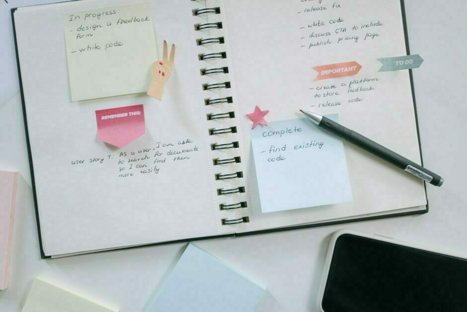 high angle shot of a notebook and a pen beside a mobile phone