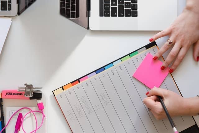 Picture showing a computer and a hand writing on a post-it note. 