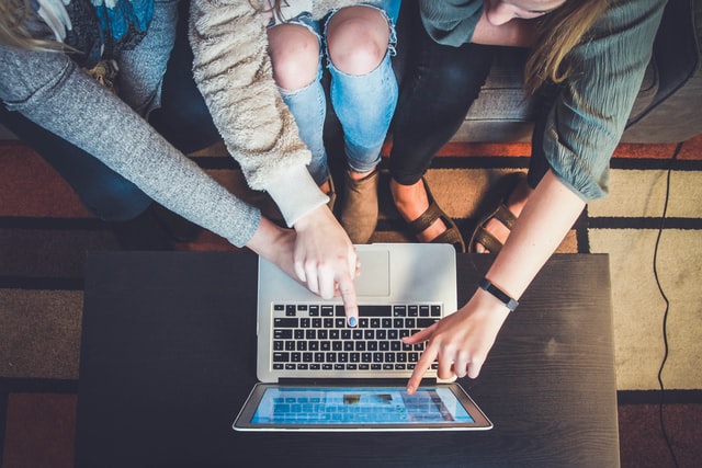 Image from above of people sitting on a couch, pointing at the screen of a laptop.