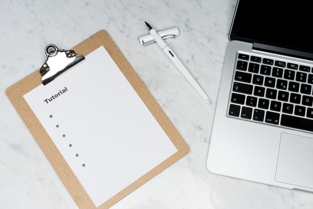 Image showing a marble desktop. On top is a clipboard with the text tutorial. You can also see parts of a laptop and a fountain pen.