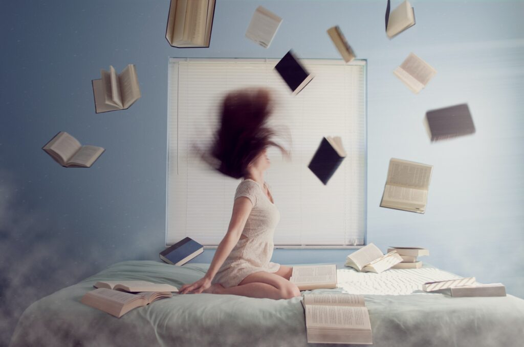 Image of a woman on a bed with books flying around the room