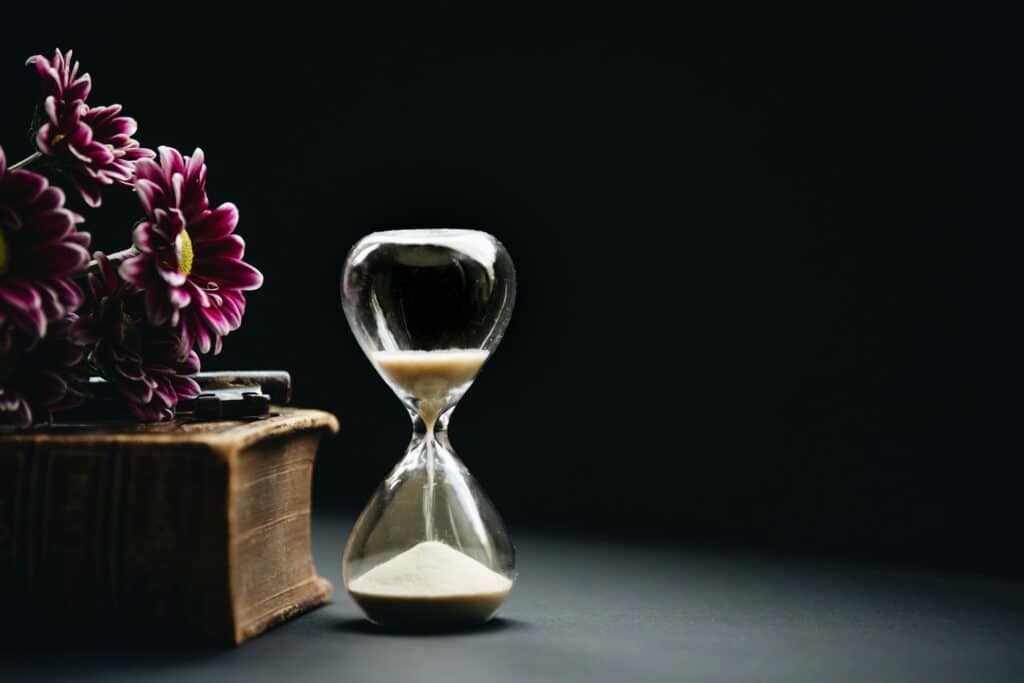 Photo showing a clear hour glass beside pink flowers.