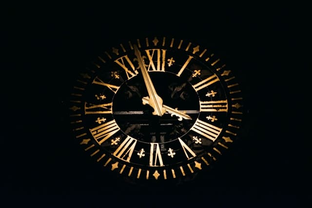 Round black and brown analog clock with roman numerals on a black background.